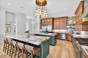 A modern kitchen with a central island, wooden cabinets, stainless steel appliances, and a chandelier.