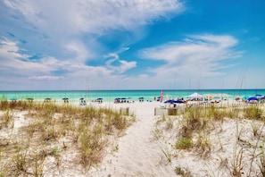 Une plage avec un sentier de sable menant à l’eau, des parasols et des chaises de plage.