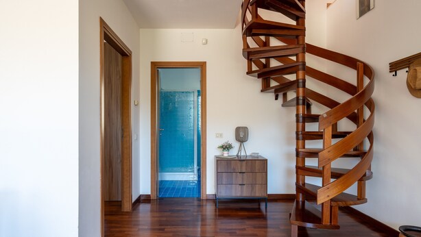 Una scala a chiocciola in un corridoio con pavimento in legno e una porta che dà su una stanza con pavimento piastrellato di blu.
