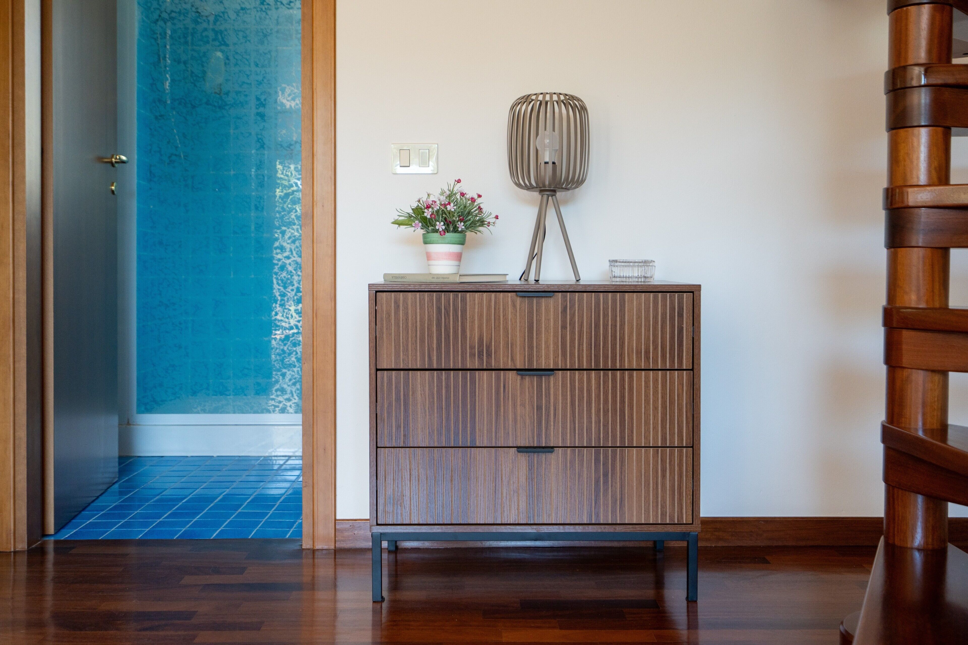 Ein Holzschrank mit Schubladen, ein Blumentopf, eine Lampe und ein kleines Regal mit Büchern.