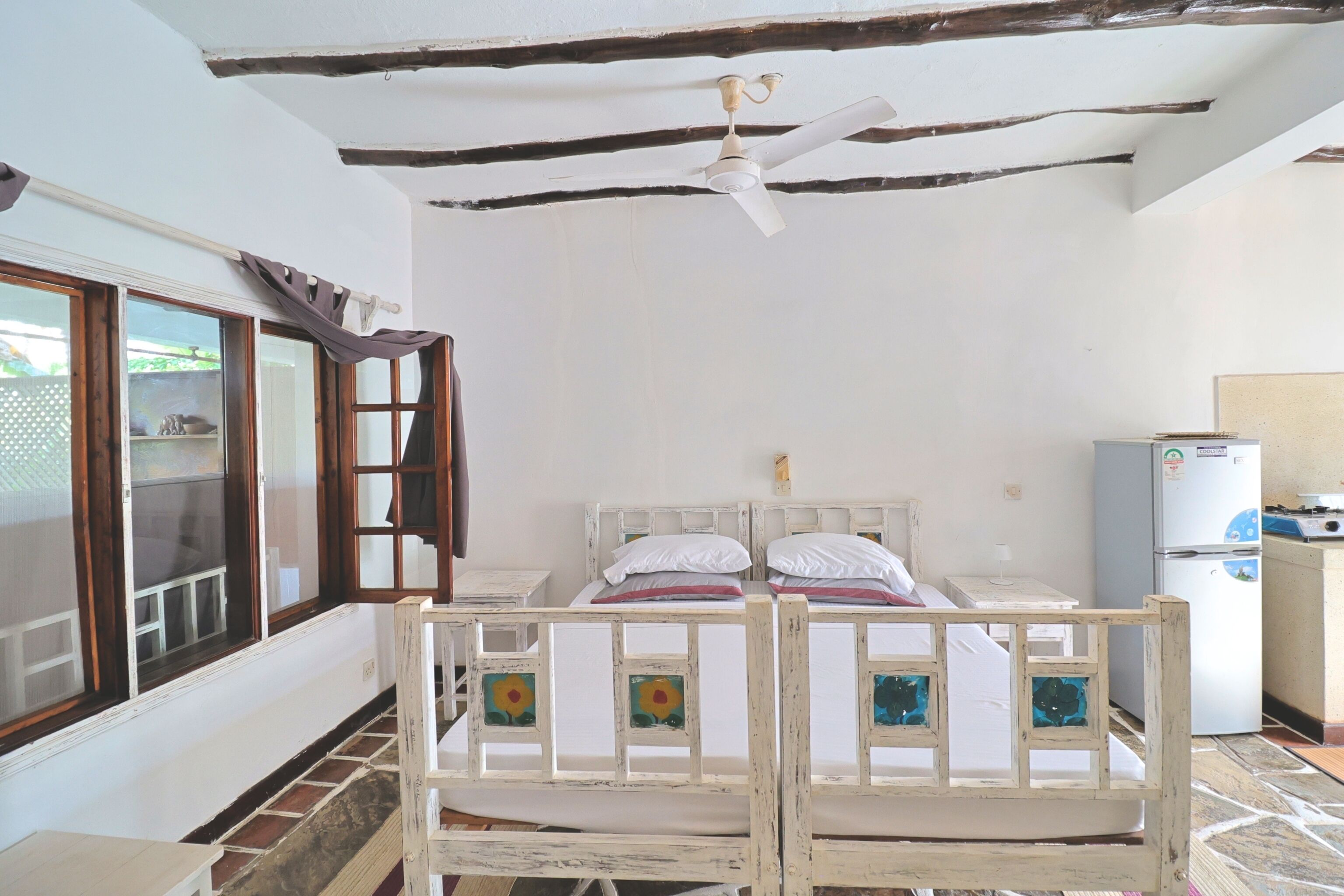 A room with a bed, a ceiling fan, a window, and a refrigerator.