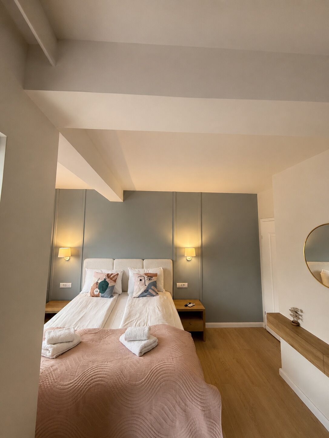 A bedroom with two beds, bedside lamps, a wooden nightstand, a mirror, and a wooden dresser.