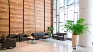 Un vestíbulo espacioso con diseño moderno, que incluye un gran panel de pared de madera, un área de estar con sofás y mesas, y ventanas amplias que permiten la entrada de luz natural.