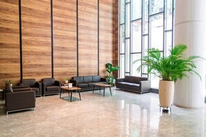 Eine großzügige Lobby mit modernem Design, mit einer großen Wand aus Holzpaneelen, einer Sitzecke mit Sofas und Tischen und großen Fenstern, die viel Tageslicht hereinlassen.