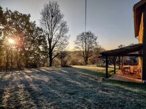 A covered outdoor seating area with a view of a frost-covered lawn and trees.