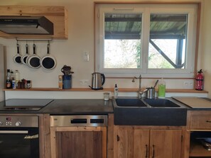 A kitchen with wooden cabinets, a stainless steel sink, a built-in oven, and a window with a view of trees.