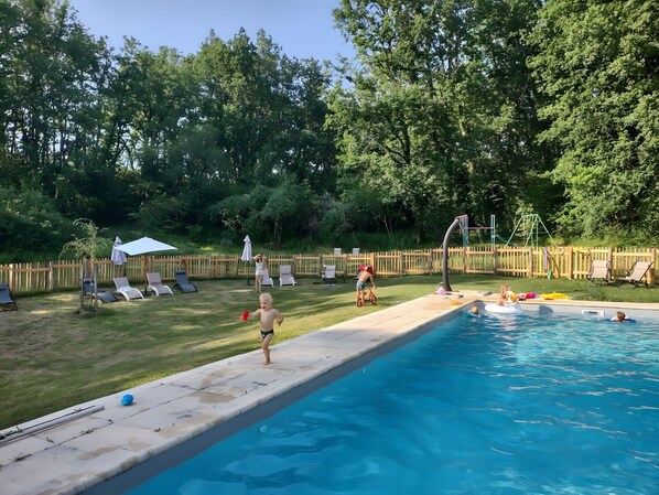 A backyard with a swimming pool, a wooden fence, and a grassy area with lounge chairs.
