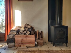A room with a fireplace, a stack of firewood, a woven basket, and a black stove.