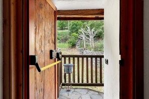 Una porta di legno con maniglia metallica, un secchio di metallo con l'indicazione 'COLD DRINKS' su un supporto, e un patio in pietra con ringhiera in legno.