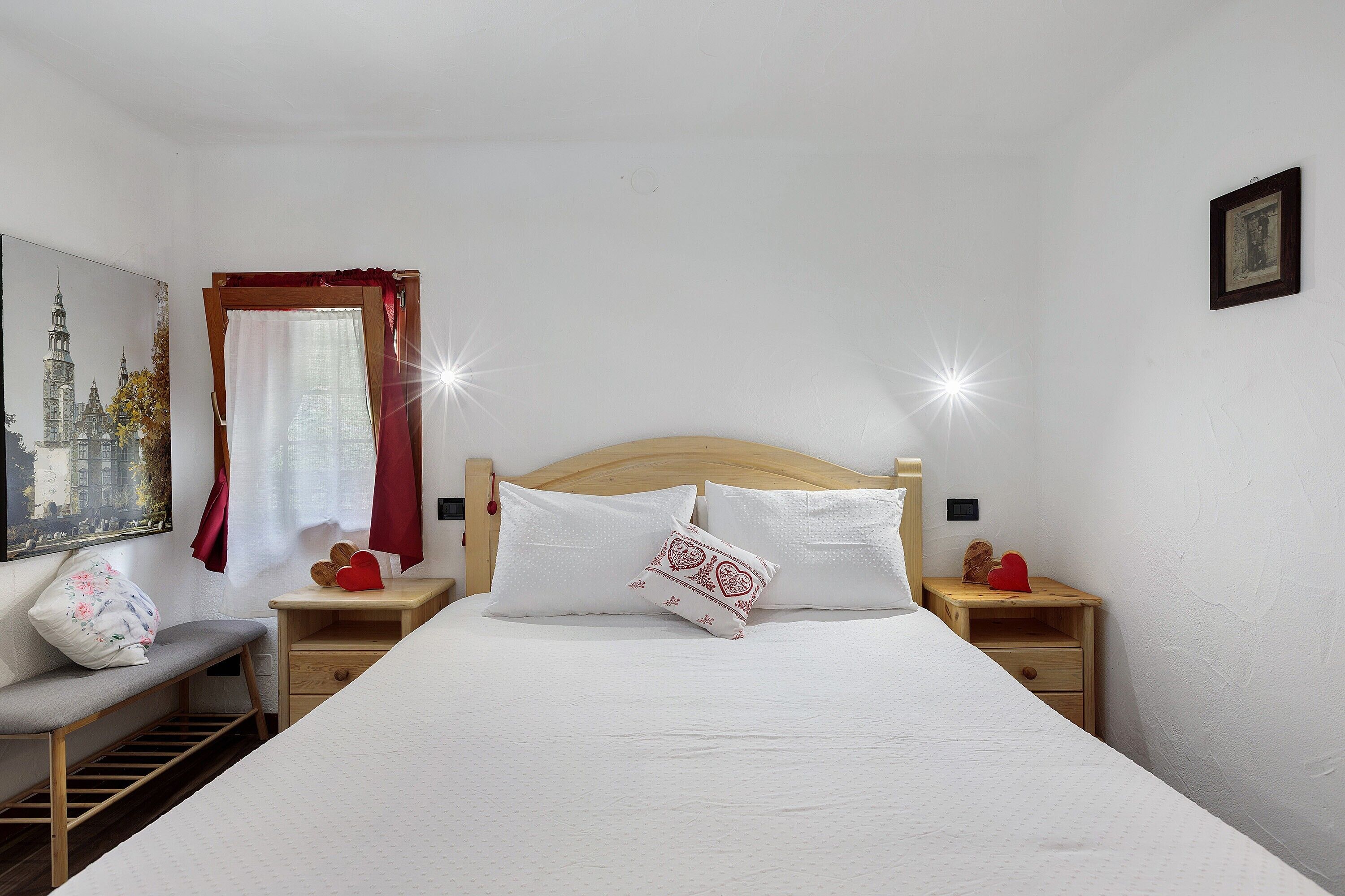 Een slaapkamer met een groot bed, een nachtkastje, een bankje en een aan de muur hangend schilderij.