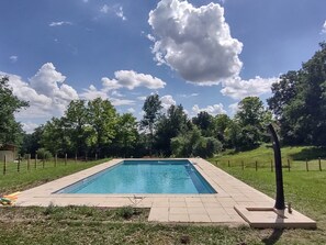 A rectangular pool with a tiled deck, surrounded by a grassy area and trees.