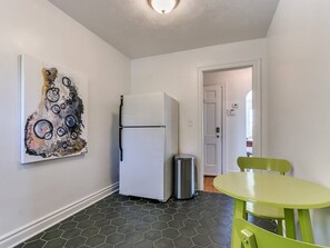 Une cuisine de taille réduite, équipée d’un réfrigérateur, d’une poubelle et d’une table verte.