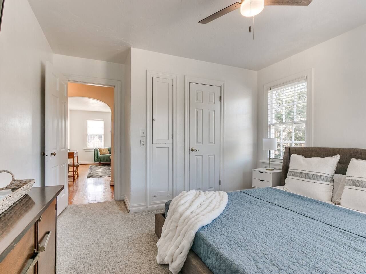 A bedroom with a bed, a nightstand, a dresser, and a door leading to another room.