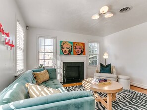 A living room with a fireplace, a sofa, a coffee table, and artwork on the wall. - Historic Crown Heights Triplex - Unit B (Oklahoma City)