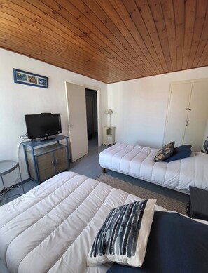 A room with two beds, a desk with a TV, a lamp, and a door leading to another room. - Little House by the Sea (Talmont-Saint-Hilaire)