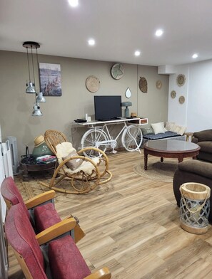 A living room with a television, white bicycle, wicker chairs, and a round coffee table. - Little House by the Sea (Talmont-Saint-Hilaire)