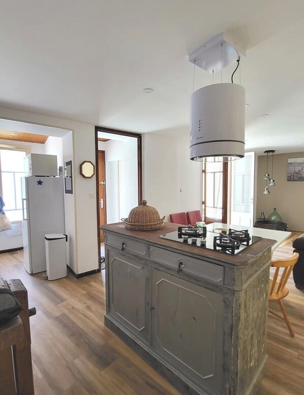 A kitchen with a central island, a refrigerator, a microwave, and a dining area with a table and chairs. - Little House by the Sea (Talmont-Saint-Hilaire)