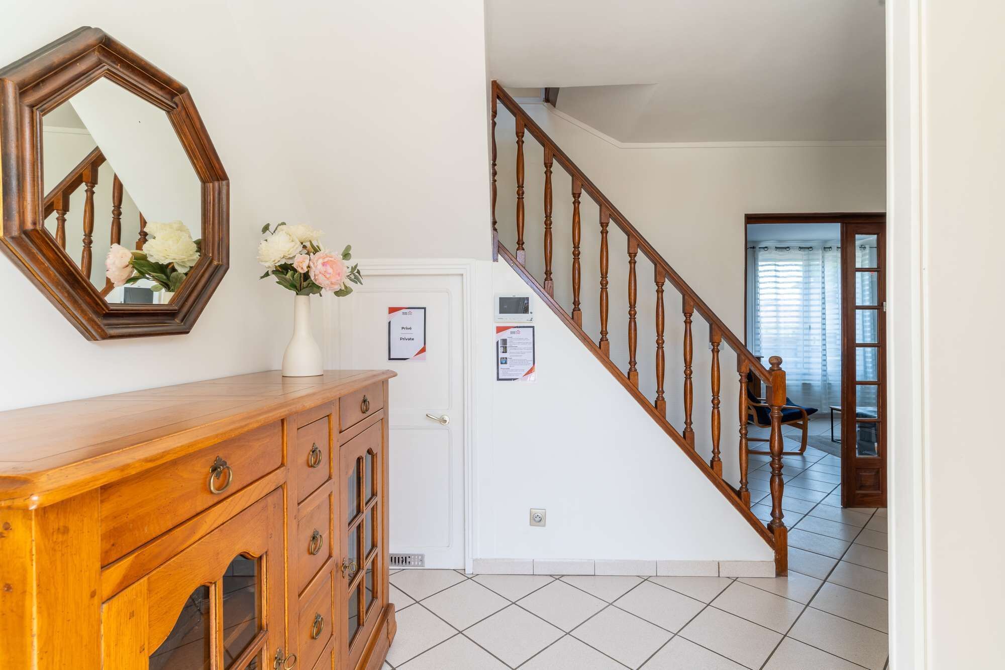 A staircase with wooden balusters, a wooden cabinet with drawers, a wall-mounted mirror, and a vase with flowers.