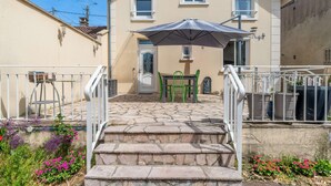 A building with a stone staircase leading to a door, a table with chairs, and an umbrella. - Entire Home · 1000m² Garden · Terrace · 30min from Paris (Conflans-Sainte-Honorine)