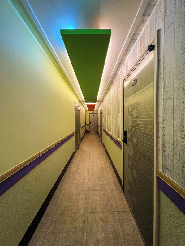 A long, narrow hallway with a green ceiling light, doors on both sides, and a tiled floor.