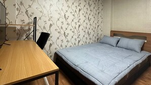 Un dormitorio con un escritorio de madera, una cama con colchón gris y papel tapiz floral.