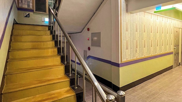 Una escalera con barandilla de metal, un muro con azulejos y una puerta al final.