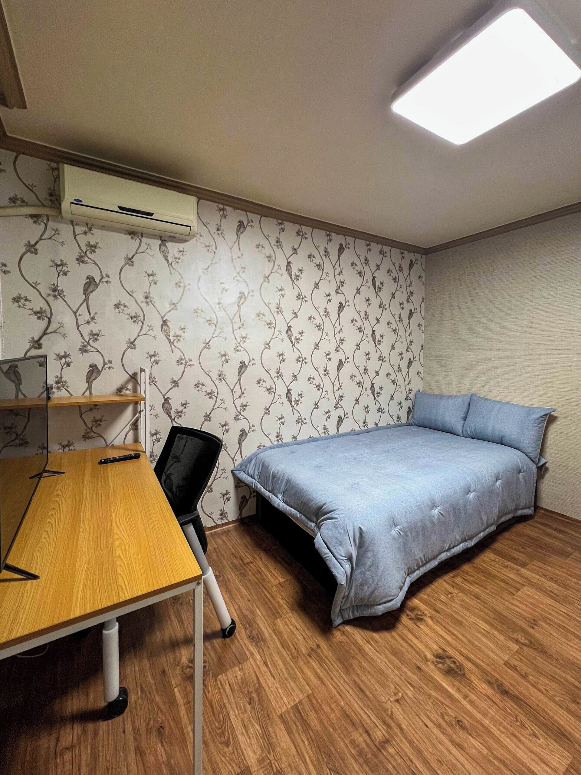 Une chambre à coucher comprenant un lit, un bureau, une chaise, un climatiseur et un papier peint à motifs.