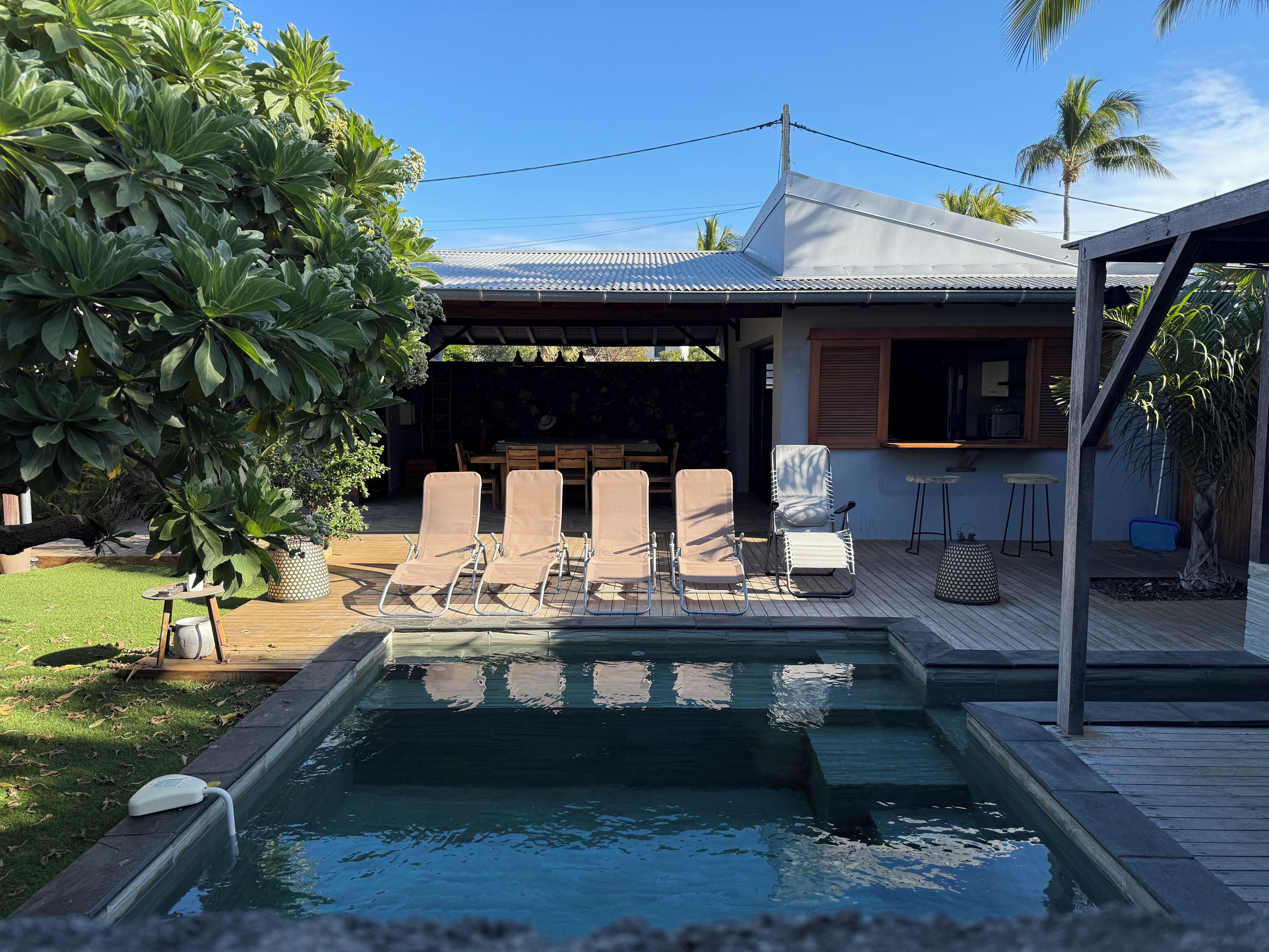 A swimming pool with lounge chairs, a covered patio, and a wooden deck.