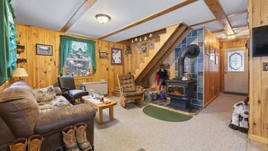 A cozy cabin interior with a wooden interior, a fireplace, a staircase, and a living area with a couch and a chair. - Stratton Camp - ATV + Snowmobile Trails - Near Sugarloaf (Stratton)
