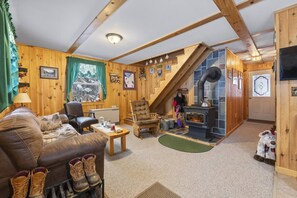 Ein gemütliches Blockhaus-Interieur mit Holzvertäfelung, Kamin, Treppe und Wohnbereich mit Sofa und Sessel.
