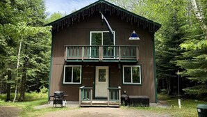 A two-story cabin with a balcony, a front door, and a small porch area. - Stratton Camp - ATV + Snowmobile Trails - Near Sugarloaf (Stratton)