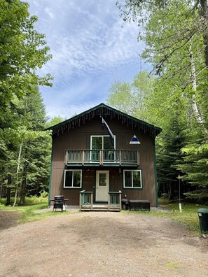 Eine zweistöckige Hütte mit Balkon, Eingangstür und kleiner Veranda.
