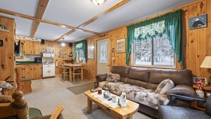 A cozy cabin interior with a dining area, a sofa, and a table with a lamp. - Stratton Camp - ATV + Snowmobile Trails - Near Sugarloaf (Stratton)