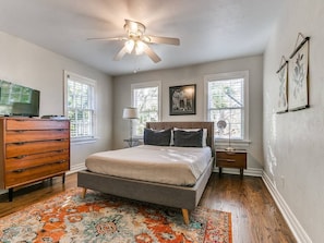 A bedroom with a bed, dresser, nightstand, lamp, ceiling fan, and windows. - Historic Crown Heights Triplex - Unit C (Oklahoma City)