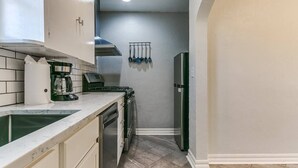 Eine kompakte Küche mit Spüle, Herd und Kühlschrank, mit weißen Schränken und einer gefliesten Rückwand.