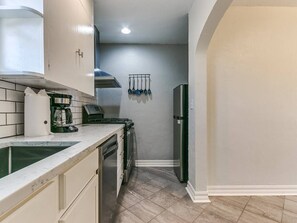 A compact kitchen with a sink, stove, and refrigerator, featuring white cabinets and a tiled backsplash. - Historic Crown Heights Triplex - Unit C (Oklahoma City)