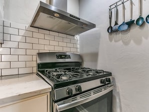 A kitchen with a gas stove, a stainless steel range hood, and a tiled backsplash. - Historic Crown Heights Triplex - Unit C (Oklahoma City)