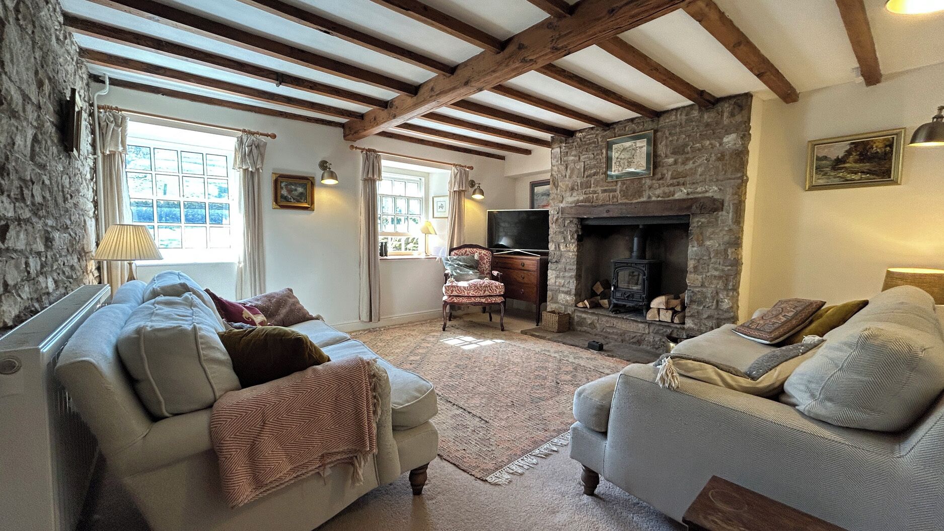 Een gezellige woonkamer met een stenen openhaard, houten balken en twee banken.