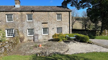 A stone building with multiple windows, a gravel driveway, and a small garden area with a table and chairs.
