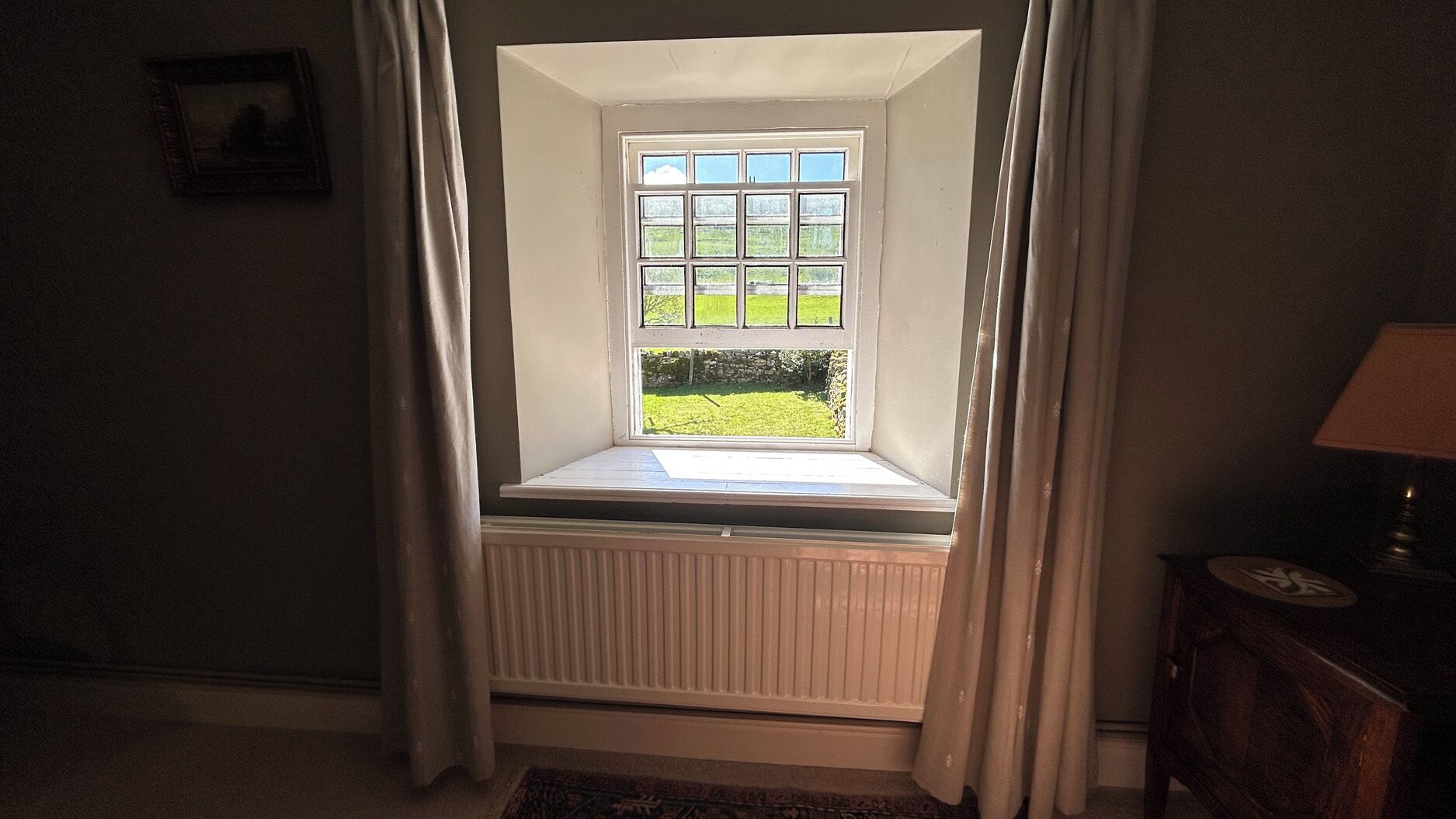 A room with a bay window, a radiator, a lamp, and a picture on the wall.