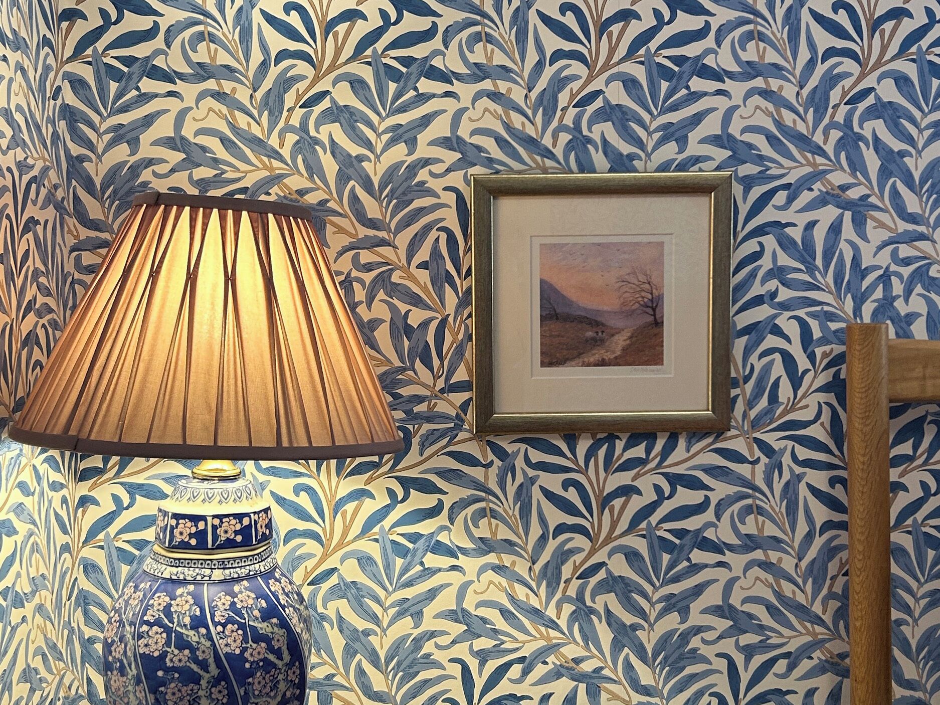 Un muro con un motivo a foglia blu e bianco, un quadro incorniciato e un vaso blu con decorazioni floreali.