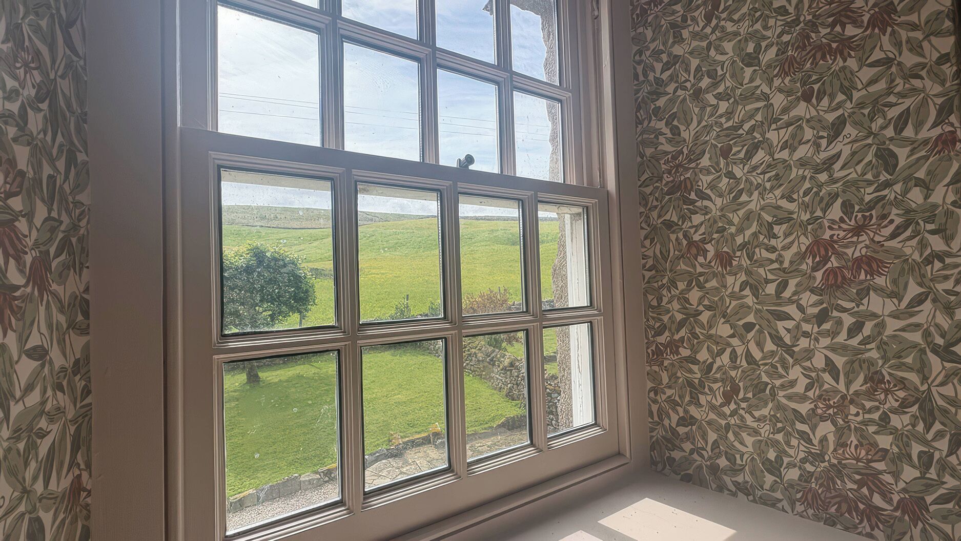 A room with a large window offering a view of a green field and a tree.