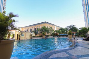 Ein Schwimmbecken mit einem Gebäude im Hintergrund, umgeben von Kübelpflanzen und Bäumen.
