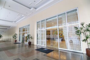 Eine geräumige Lobby mit großen Glasüren, Topfpflanzen und einem gefliesten Boden.