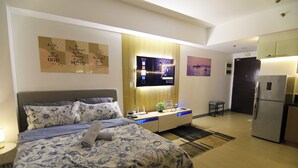 A modern hotel room with a bed, bedside table, TV, and a kitchenette. - Venice Luxury Residences with direct access to Venice Mall, near BGC & Airport (Taguig)