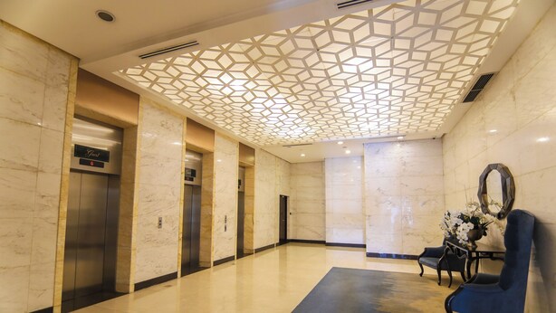 A lobby with marble walls, a geometric ceiling design, an elevator, and a blue chair. - Venice Luxury Residences with direct access to Venice Mall, near BGC & Airport (Taguig)