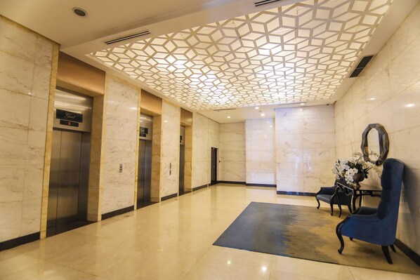 A lobby with marble walls, a geometric ceiling design, an elevator, and a blue chair. - Venice Luxury Residences with direct access to Venice Mall, near BGC & Airport (Taguig)