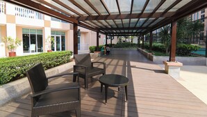 An outdoor covered patio area with wicker furniture, a small round table, and a seating arrangement. - Venice Luxury Residences with direct access to Venice Mall, near BGC & Airport (Taguig)