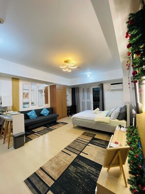 A modern hotel room with a bed, a sofa, a desk, and a small dining area. - Cozy Condo with Access to Venice Grand Canal Mall, near BGC & Airport (Taguig)