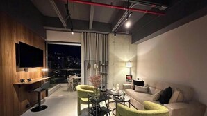 Een moderne woonkamer met een bank, fauteuils, een televisie en uitzicht over de stad.